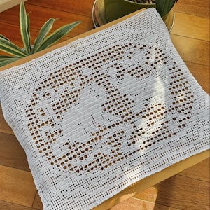 Könnte beinhalten: Rechteckige, cremefarbene Häkeldecke mit floralem Muster. Sie liegt auf einer hellbraunen Oberfläche, mit einem Holzboden im Hintergrund. Das Häkelwerk weist Lochmuster und einen detaillierten Rand auf. Ungefähr 40 cm x 50 cm.