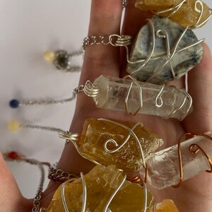 May include: Five wire-wrapped crystal necklaces with different colored stones. The necklaces are made with silver and copper wire. The stones are clear quartz, citrine, and a grey stone.