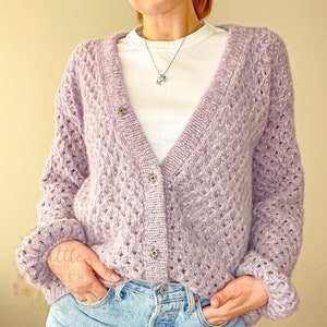 Può includere: Un cardigan color lilla chiaro con un delicato motivo traforato e chiusura con bottoni. Il cardigan è realizzato in un filato morbido e soffice e ha una vestibilità rilassata.