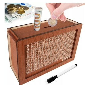 Può includere: Un salvadanaio di legno con uno slot nella parte superiore e una griglia sul davanti che mostra l'importo del denaro risparmiato. La griglia mostra denominazioni da 5 centesimi a 200 euro. La scatola ha un pennarello bianco accanto e il testo "10.000 €" è stampato sul davanti.