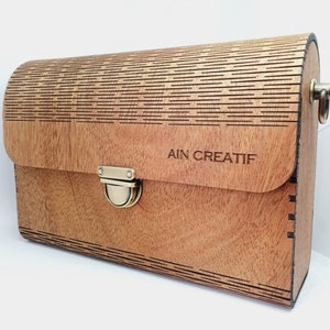 May include: A wooden handbag with a brass clasp and a laser-cut design. The bag has the text "AIN CREATIF" engraved on the front.