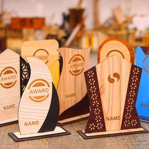 May include: Five wooden award plaques with different designs. The plaques are made of light brown wood with dark brown accents. The plaques have the words "Award" and "Name" engraved on them. The plaques are all different shapes and sizes.