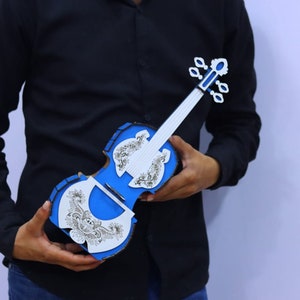 May include: A blue and white wooden violin with intricate floral designs. The violin is being held by a person wearing a black shirt.