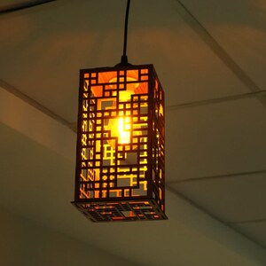 May include: A brown wooden pendant light with a geometric design. The light is on and casting a warm glow.