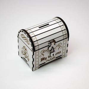 Può includere: Cassaforte in legno bianco con una serratura dorata e le parole "I miei tesori" incise sul davanti.