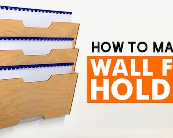 Peut inclure: Un porte-fichiers mural en bois avec quatre compartiments. Le porte-fichiers est en bois clair et a une finition naturelle. Les compartiments sont étiquetés avec des languettes bleues. Le texte "HOW TO MAKE A WALL FILE HOLDER" est affiché en lettres blanches sur un fond orange.