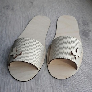 May include: A pair of wooden slippers with a butterfly design. The slippers are light brown and have a textured surface.