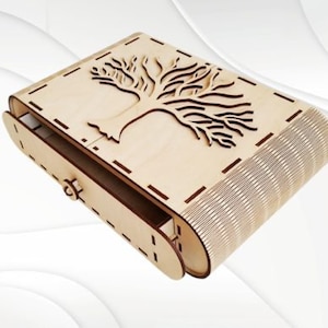 Puede incluir: Una caja de madera con un cajón y un diseño de árbol cortado con láser en la tapa. La caja está hecha de madera clara y tiene un acabado natural.