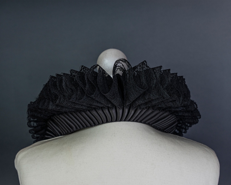 May include: A black lace ruffle collar with a pleated fabric backing. The collar is displayed on a white mannequin.