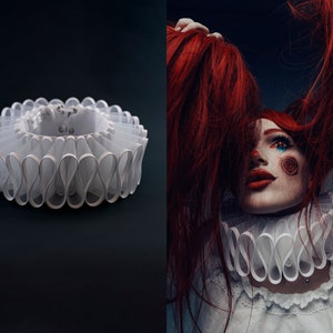 Könnte beinhalten: Ein weißer Rüschenkragen mit geschichtetem Design, neben einer Person mit roten Haaren und Clown-Make-up. Der Kragen besteht aus einem transparenten Stoff und hat eine kreisförmige Form. Die Person trägt einen passenden Kragen.