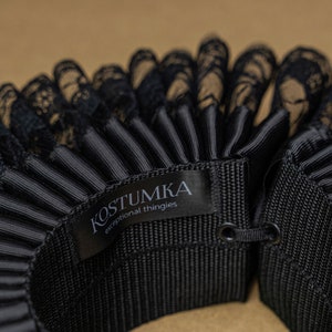May include: Black lace and black satin ruffled collar with a black label that reads "KOSTUMKA exceptional thingies".