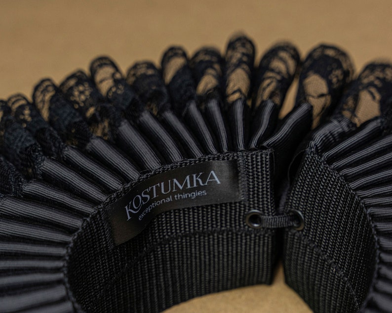 May include: Black lace and black satin ruffled collar with a black label that reads "KOSTUMKA exceptional thingies".