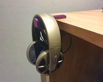 May include: Gold-colored over-ear headphones with black earcups hanging from a purple headphone stand. The headphones are labeled "HD 485". The stand is mounted on the edge of a wooden table.