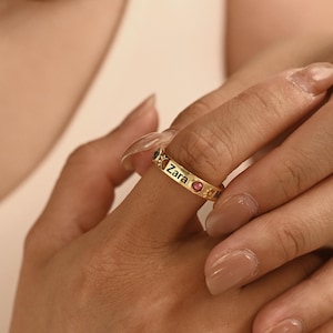 Puede incluir: Un anillo dorado con el nombre "Zara" grabado y pequeñas piedras preciosas. El anillo se lleva en un dedo. Es una pieza de joyería.
