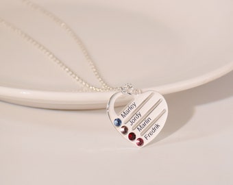 May include: Silver heart-shaped necklace with a chain. The heart has five lines engraved with the names Marley, Jordy, Marlin, and Fredrik. Each name has a small gemstone next to it.