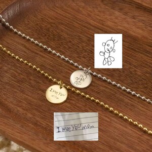 Peut inclure: Deux bracelets délicats à chaîne boule, l'un doré et l'autre argenté, chacun avec un pendentif rond. L'un des pendentifs dit "I love you mom", l'autre porte le dessin d'un ours. Une note manuscrite dit "I love you mom".