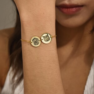 Puede incluir: Un brazalete de cadena dorada con dos dijes redondos que presentan im&aacute;genes grabadas de un gato y un perro.