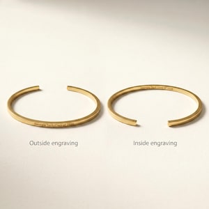 May include: Two gold-colored, open-ended bracelets. One bracelet has "Georgia Tech Class of 2026" engraved on the outside, the other on the inside. The bracelets are displayed on a white surface.