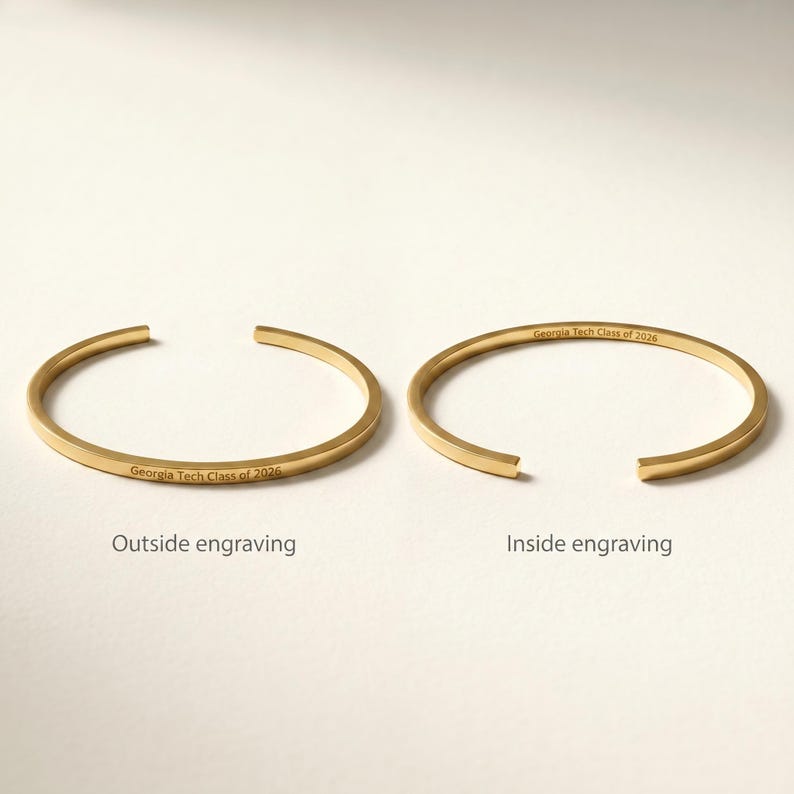 May include: Two gold-colored, open-ended bracelets. One bracelet has "Georgia Tech Class of 2026" engraved on the outside, the other on the inside. The bracelets are displayed on a white surface.
