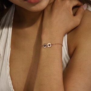 Puede incluir: Un brazalete de cadena de oro rosa con dos peque&ntilde;os dijes redondos. Un dije tiene un dise&ntilde;o de huella de pata y el otro dije es liso.