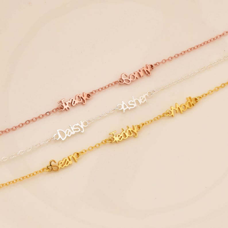 May include: A collection of delicate name bracelets in rose gold, silver, and gold. Each bracelet features a different name in a cursive font: Tracy, Sonny, Daisy, Asher, Sean, Teddy, and Mollie. The bracelets are displayed on a light pink background.