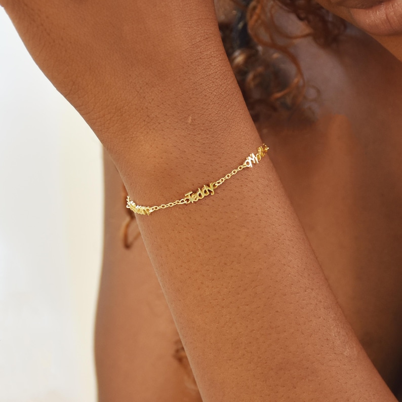 May include: A delicate gold-colored bracelet spelling out the name "Teddy" in cursive script. The bracelet is worn on a wrist, showcasing its fine chain and personalized design. The bracelet is a piece of jewelry.