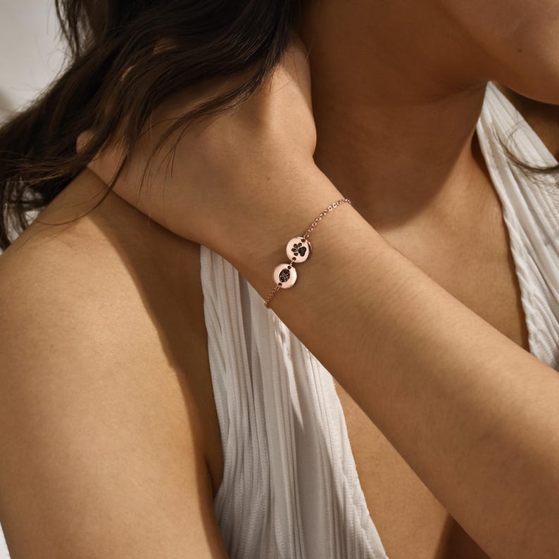 Puede incluir: Un brazalete de cadena de oro rosa con dos dijes redondos con huellas de patas. Los dijes est&aacute;n conectados a la cadena con peque&ntilde;os anillos.