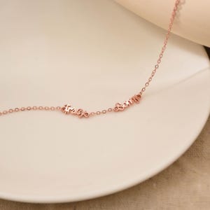 May include: Rose gold necklace with the words "Free" and "Sorry" in a delicate cursive font. The necklace is displayed on a white plate, showcasing its elegant design and fine craftsmanship. The chain is thin and the letters are small.