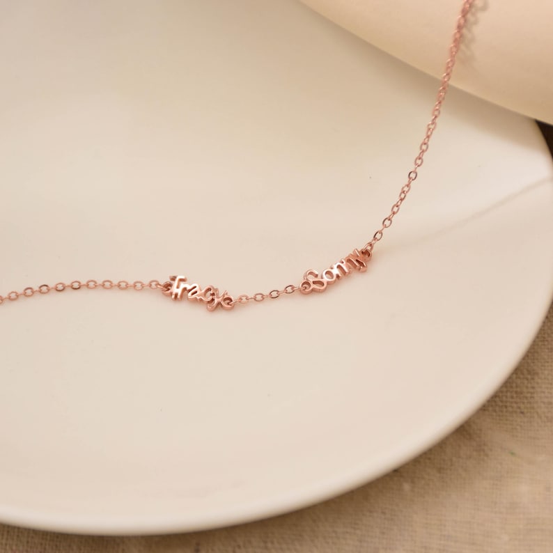May include: Rose gold necklace with the words "Free" and "Sorry" in a delicate cursive font. The necklace is displayed on a white plate, showcasing its elegant design and fine craftsmanship. The chain is thin and the letters are small.