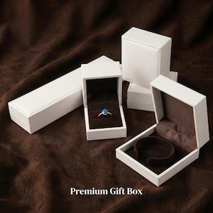 May include: Several white jewelry boxes, some open to reveal a ring and a bracelet holder. The ring has a gold band and a blue gemstone. The boxes are on a brown surface. Text on the bottom reads "Premium Gift Box".