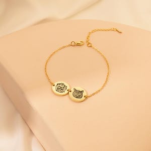 Puede incluir: Un brazalete de cadena dorada con dos dijes redondos con im&aacute;genes grabadas de un perro y un gato.