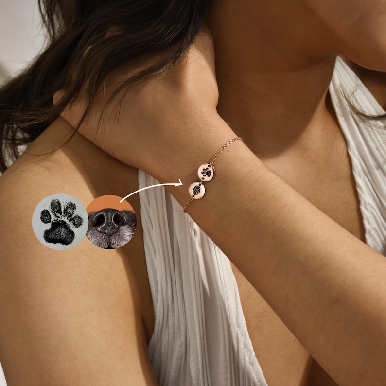Puede incluir: Un brazalete de cadena de oro rosa con dos dijes redondos con huellas de patas. Los dijes est&aacute;n grabados con una huella de pata negra y una huella de nariz marr&oacute;n.