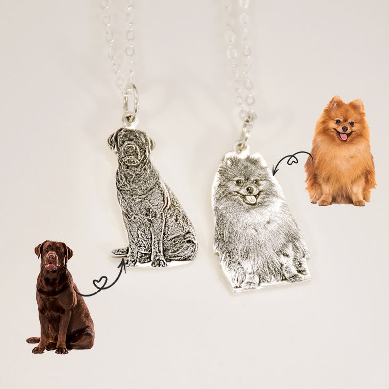 May include: Two silver necklaces with dog portraits. One necklace features a black Labrador Retriever, the other a brown Pomeranian.