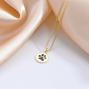 May include: Gold necklace with a round pendant featuring a black paw print.