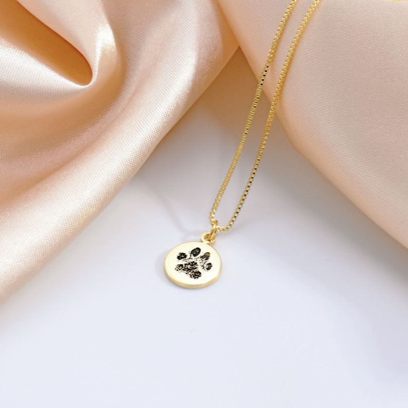 May include: Gold necklace with a round pendant featuring a black paw print.