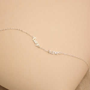 May include: A delicate silver necklace with the names "Daisy" and "Asher" in cursive script. The necklace features a fine chain and is displayed against a neutral background. A personalized jewelry item.