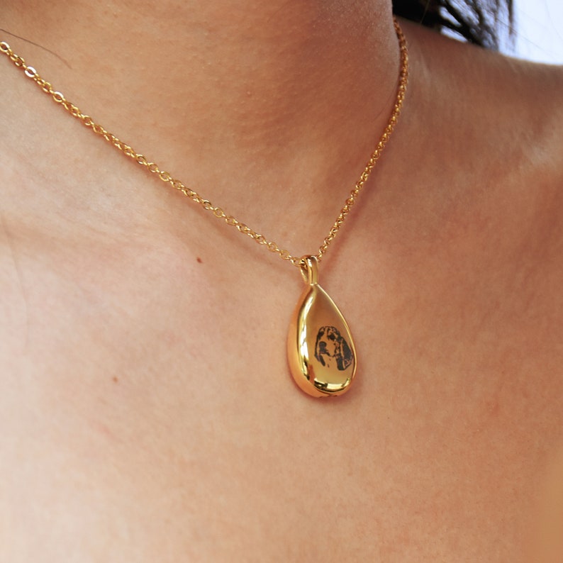 May include: A gold teardrop-shaped pendant necklace with a black and white image of a dog's face inside.