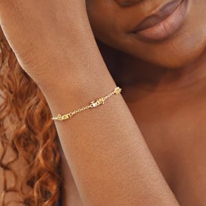 May include: A delicate gold bracelet with the names "Sean" and "Teddy" spelled out in cursive script. The bracelet is attached to a chain and is worn on a wrist. The bracelet is a piece of jewelry.