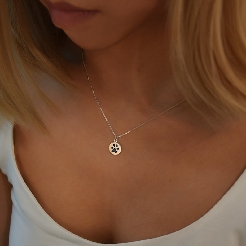 May include: A silver necklace with a small, round pendant featuring a black paw print.