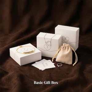 May include: A collection of jewelry gift boxes and accessories on a brown background. The image includes white boxes with heart designs, a gold bracelet, a silver necklace, a small beige pouch, a ring, and cards that say "Best Wishes". The text "Basic Gift Box" is at the bottom.