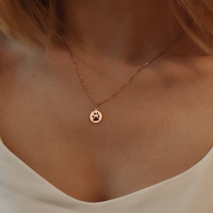 May include: A rose gold necklace with a small, round pendant featuring a cut-out paw print design.
