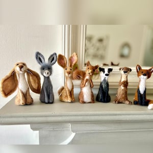 Seven character needle felted animals standing in a line. There is a hare with droopy ears, a donkey, hare with upright ears, squirrel, badger, otter and fox.