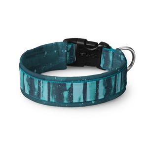 May include: Teal and turquoise dog collar with a black plastic buckle and a silver metal D-ring. The collar features a watercolor-style pattern with vertical stripes and white speckles. The collar is designed for pets.