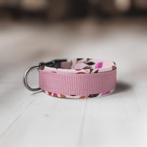 May include: A pink dog collar with a floral pattern and a black buckle. The collar is made of a soft, durable material and is designed to be comfortable for your pet.