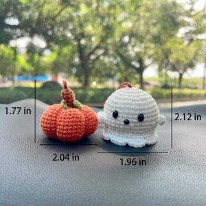 May include: Crocheted Halloween decorations: an orange pumpkin (2.04 in. wide, 1.77 in. tall) and a white ghost (1.96 in. wide, 2.12 in. tall). The pumpkin has a green stem and a brown top. The ghost has black eyes and a small loop for hanging.