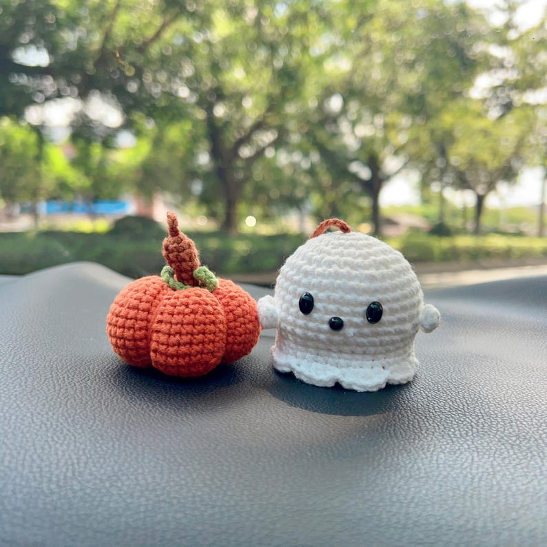 May include: Two crochet Halloween decorations: an orange pumpkin and a white ghost. The pumpkin has a green stem and a brown top. The ghost has black eyes and a small loop for hanging. These handmade items are perfect for seasonal decor.