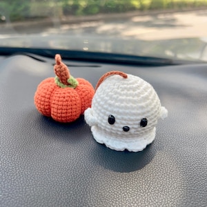 May include: Two handmade crochet Halloween decorations: an orange pumpkin with a green stem and a white ghost with black eyes. The pumpkin has a brown stem and the ghost has a brown string attached. These are perfect for seasonal decor.