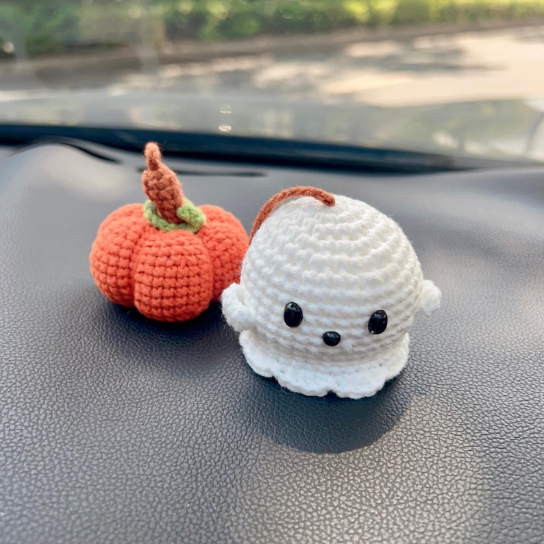 May include: Two handmade crochet Halloween decorations: an orange pumpkin with a green stem and a white ghost with black eyes. The pumpkin has a brown stem and the ghost has a brown string attached. These are perfect for seasonal decor.