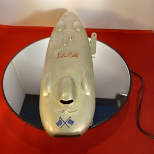 以下が含まれることがあります： ジョン・コールと赤い文字で書かれた銀色の飛行機のおもちゃ。青と白の交差した旗のデザイン。