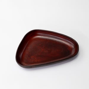 May include: A wooden tray with a unique, asymmetrical shape. The tray is a rich, dark reddish-brown color, with a smooth, polished surface. The edges are slightly raised, creating a shallow bowl. This tray is ideal for serving or displaying small items.